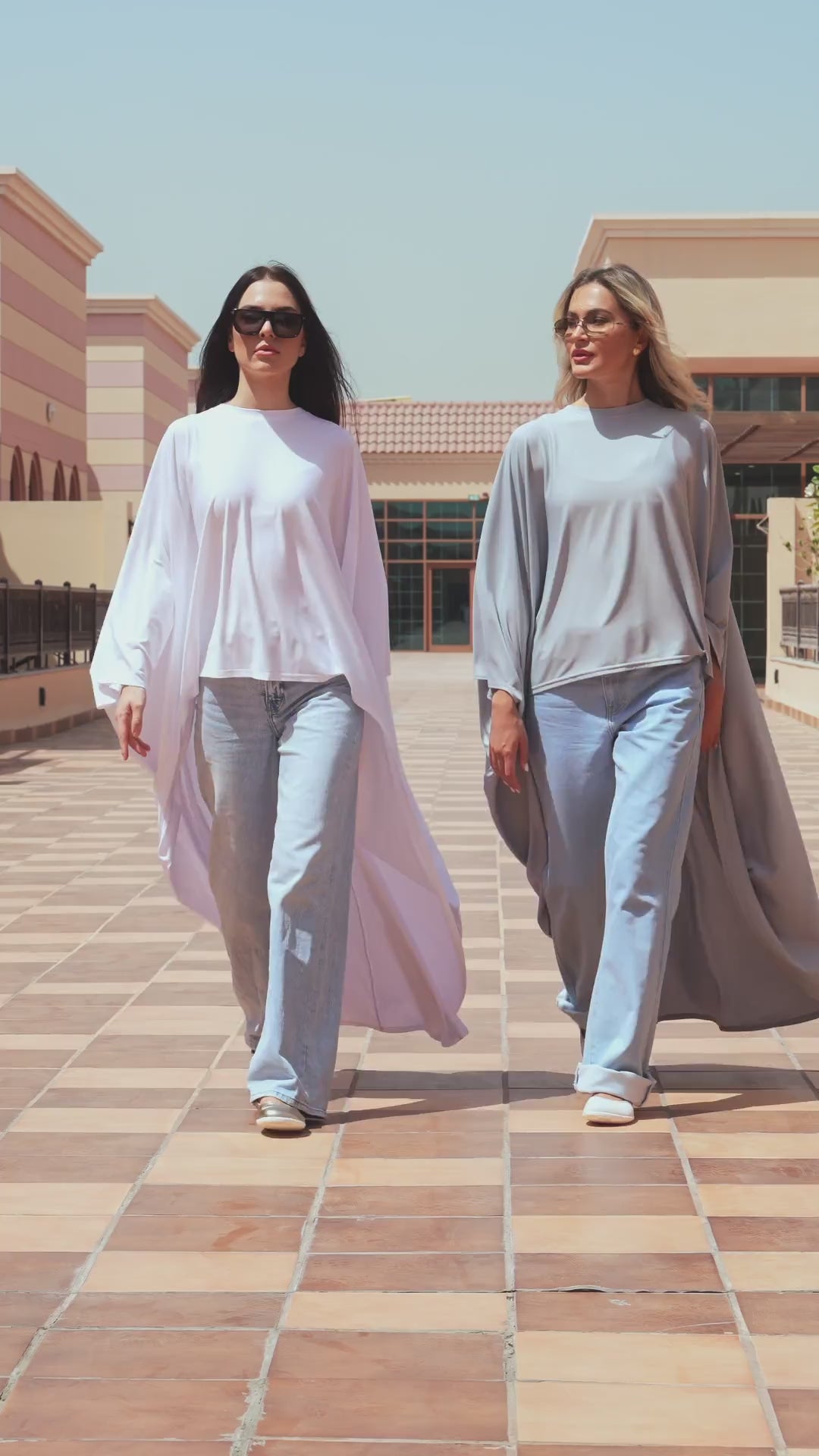 Two women walking outdoors in flowing cape tops and wide pants