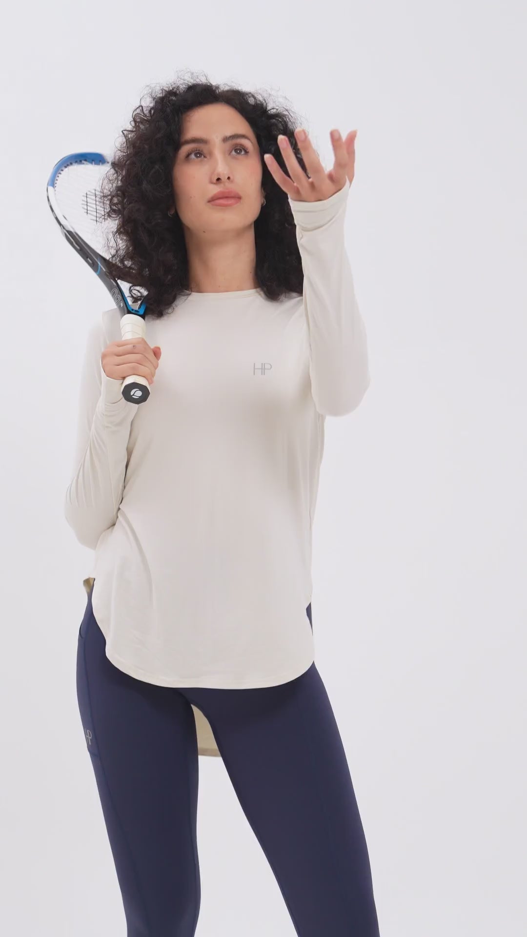 Woman playing tennis in a cream long modest top and navy leggings