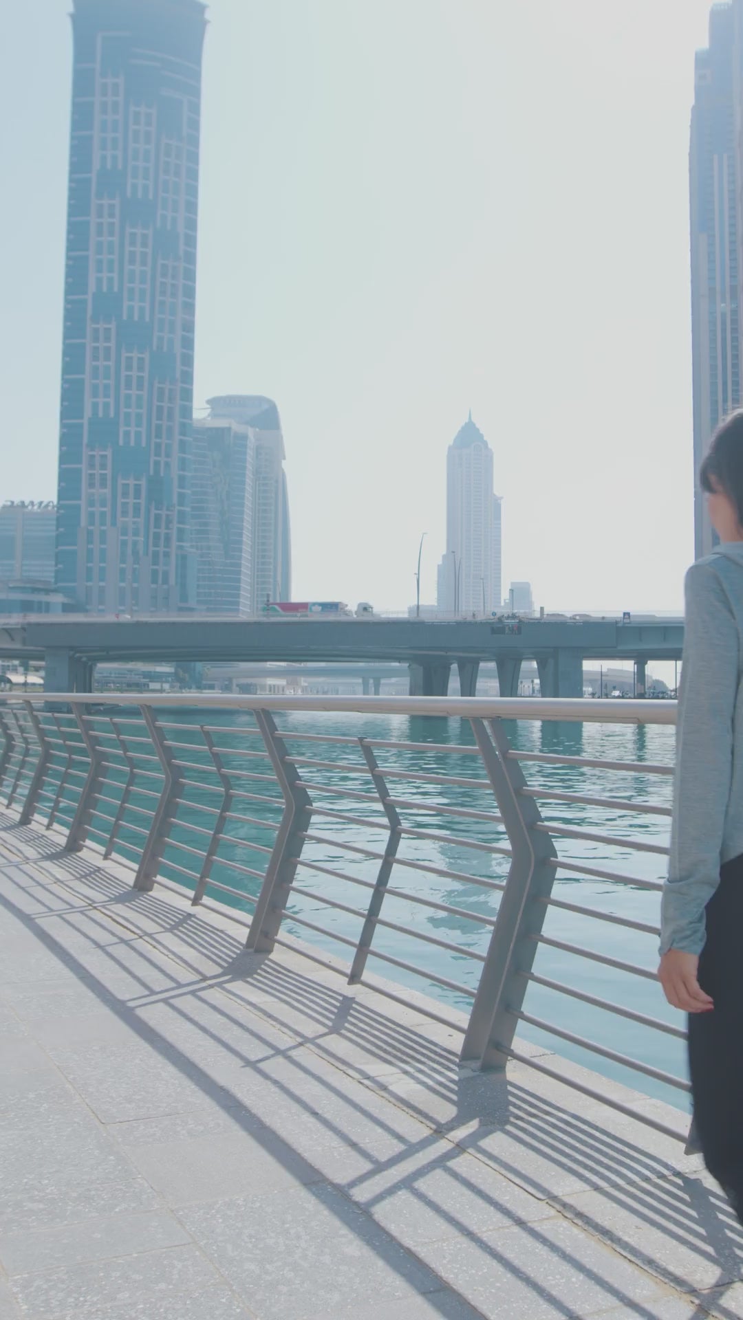 Woman stretching by the water in Dubai in a cropped-back hoodie and leggings