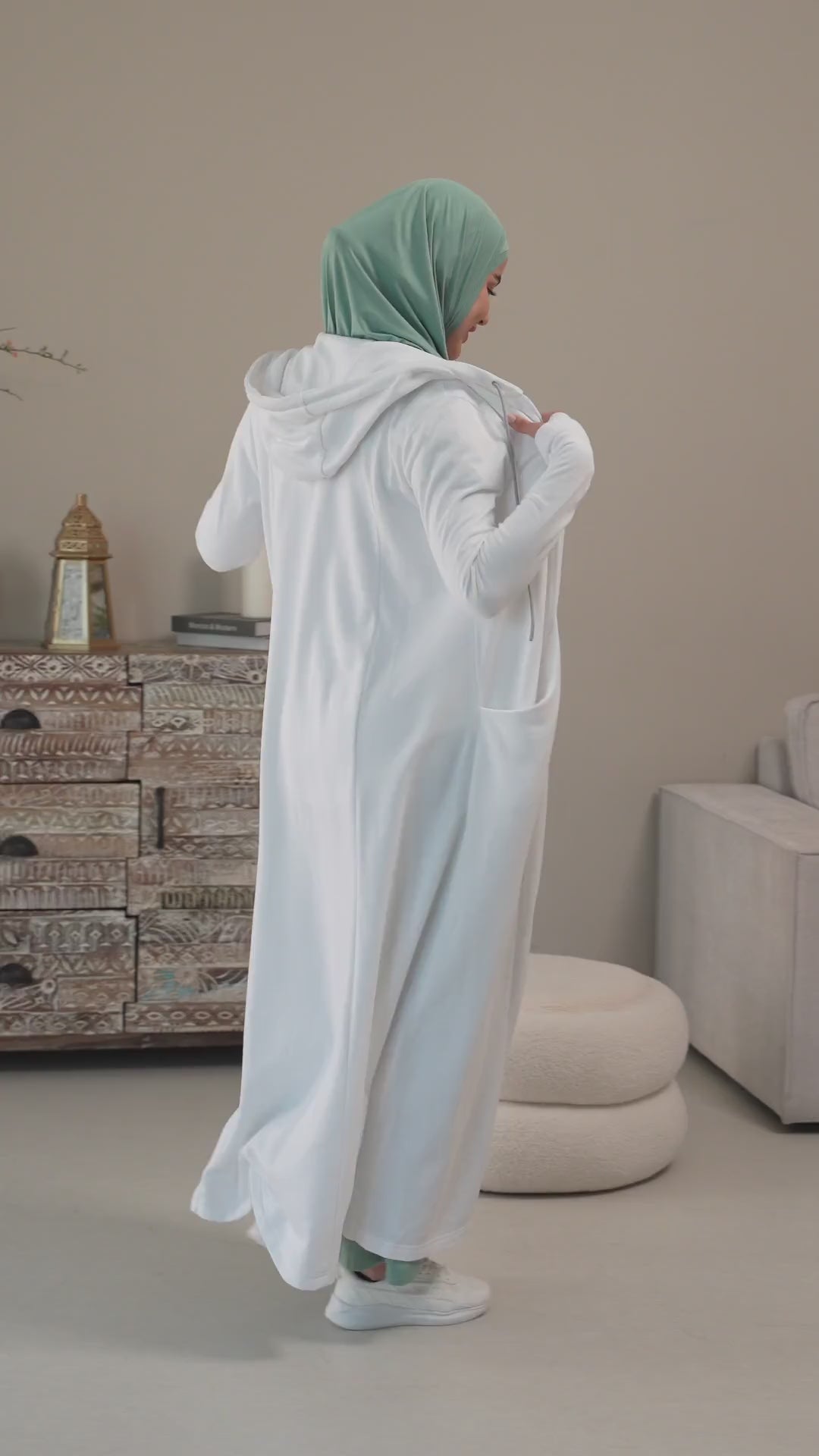 Woman in a green hijab, white ruffle-shoulder top and mint wide pants at home