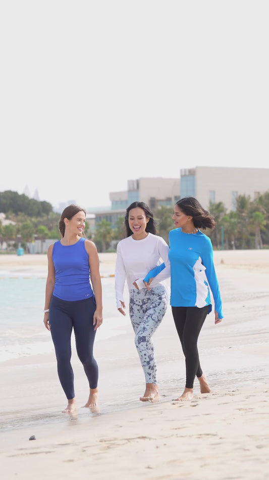 Three women walking on the beach in long modest tops, tank tops and leggings